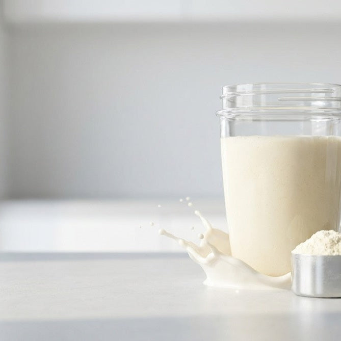 Cremiger Whey-Isolat-Shake neben einem Messlöffel mit feinem Proteinpulver auf hellem Studiohintergrund